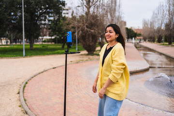 Young woman vlogger recording video for social media using smartphone on tripod in a city park