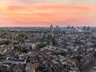 Obraz premium Aerial view of Utrecht, Netherlands, featuring the Dom Tower, historic buildings with red rooftops, green spaces, and modern high rises at sunset.