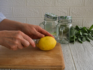Women's hands cut a lemon lengthwise on a kitchen board.