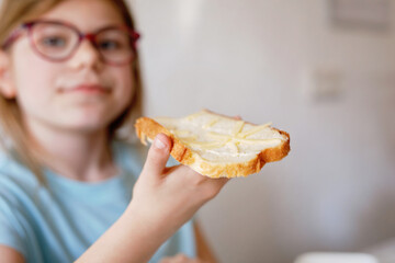 Little school girl eating bread with butter for breakfast. Happy cute child with eyeglasses having healthy snack.