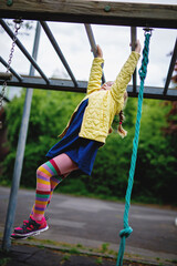 Little girl doing gymnastics on a climbing frame, horizontal bar on school yard. Child enjoying school break.