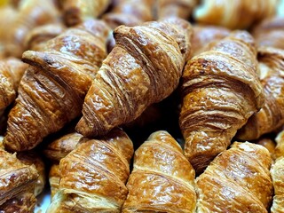 A pile of golden-brown, flaky croissants fills the frame, showcasing their crisp, layered texture and warm, appetizing color.

