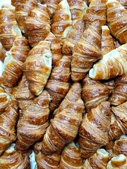 A large pile of perfectly baked, golden-brown croissants fills the frame. The flaky, layered pastry has a rich, crisp texture, ready for a delicious breakfast.
