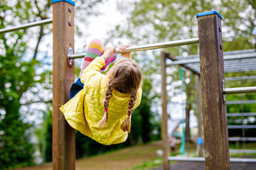 Little girl doing gymnastics on a climbing frame, horizontal bar on school yard. Child enjoying school break.
