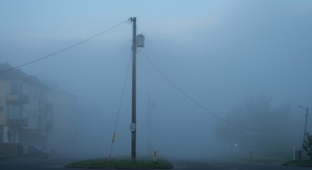 A foggy morning scene with power lines and obscured buildings, creating an eerie atmosphere.