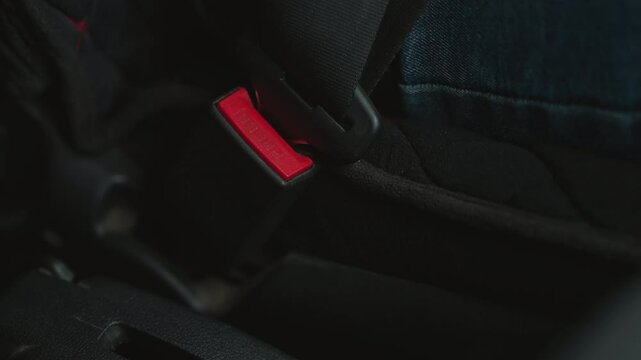 Close up of young adult hand locking seat belt buckle in car cabin focusing on finger pressing red latch under ambient lighting highlighting safety gesture and buckle mechanism detail
