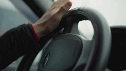 Close up hand view of driver turning steering wheel in smooth professional motion with blurred tree lined road visible through window reflection, emphasis on precise hand grip and wheel texture