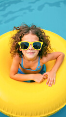 Happy caucasian child enjoying summer in pool with yellow float and sunglasses