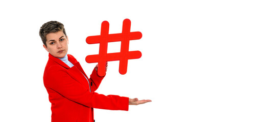Person in a red jacket holds a large red hashtag symbol against a plain white background during a...
