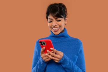 Woman smiling while texting on her smartphone against a solid background, showing engagement and...