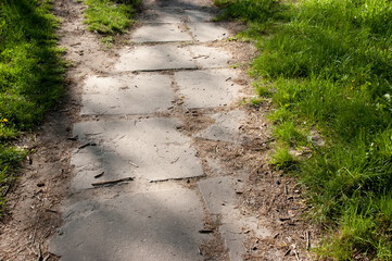 Old cracked walkway made of scattered tiles leads into the distance, with green grass growing along...