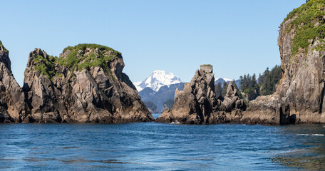 Naklejka premium A view from the water of rock formations and a snow covered mountain in the distance in Alaska