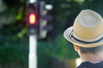 Summer walk in the city: a man in a hat stands still at a red pedestrian light. Person waits calmly...