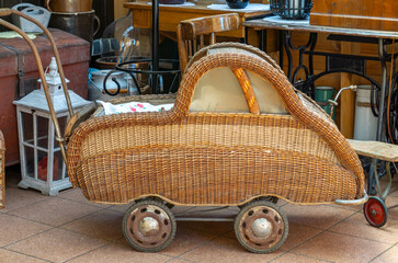 Vintage wicker baby stroller shaped like a car, displayed among antiques. A stylish retro item...