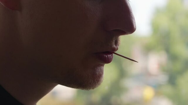 A wooden toothpick in a man's mouth.
An adult man using a toothpick.
Toothpick and oral hygiene.
Dental health