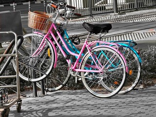 Obraz premium Two colorful vintage bicycles, one pink with a basket and one blue, are parked side-by-side, suggesting eco-friendly transport and city life.