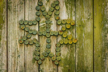 A rustic green wooden barn door with weathered paint, metal reinforcements, and a decorative bottle cap cross, set in a stone and brick wall.