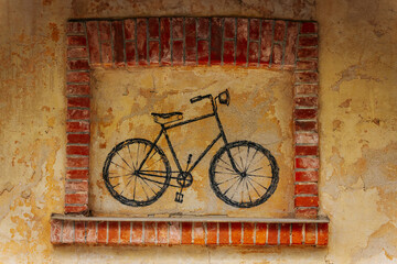 Simple black bicycle mural painted on a weathered yellow wall, framed with red bricks, creating a...