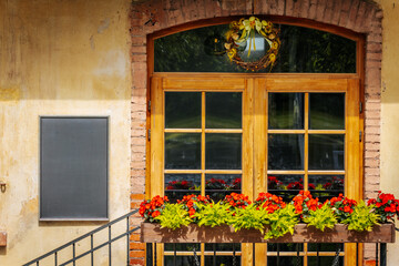 Charming restaurant facade with wooden-framed windows, red flowers in a planter, a decorative wreath.