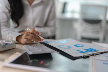 Businesswoman working with financial data using calculator and digital tablet, analyzing charts and graphs