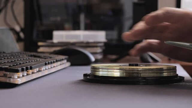 Vintage workspace with hand organizing CD cases near keyboard, retro tech and media archive vibes.
