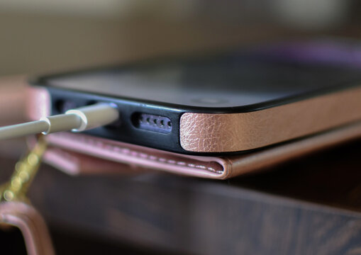 Smartphone in a pink case connected to a charger, charging on a wooden table.

