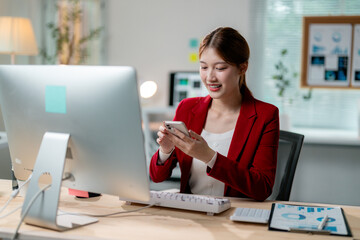 Obraz premium Young manager smiling and using mobile phone while working at her desk in modern office