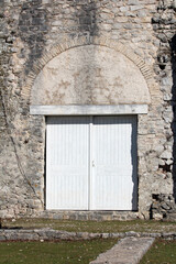 Historic stone wall features an arched lintel above closed double white wooden doors, blending...