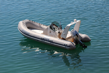 A sleek inflatable motorboat with steering console and outboard engine floats alone on tranquil blue water, reflecting sunlight and gentle waves