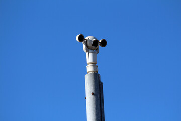 A trio of security cameras mounted on a high metal pole points in different directions, monitoring...