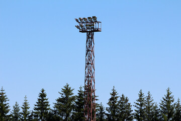 A towering metal floodlight structure rises above dense spruce trees picea abies, set against a...