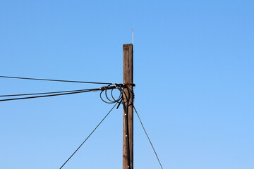 A weathered wooden utility pole supports a web of tangled electrical wires, silhouetted against a...
