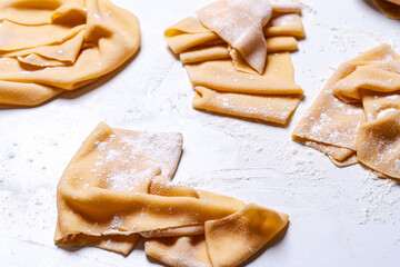 Pasta dough rolled out for naming on a white table. The process of making handmade spaghetti.