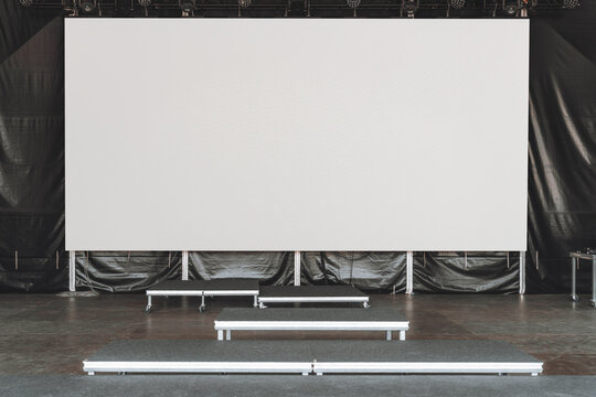 Large blank LED screen or digital billboard mockup set up on an indoor stage with empty risers and black curtains, perfect for inserting custom visuals, event branding, or advertising content