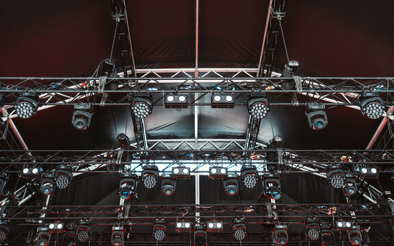 Close-up view of a dense lighting grid structure with an array of mounted LED wash lights, moving head fixtures, and trusses under a dark stage canopy, prepared for a high-energy live event