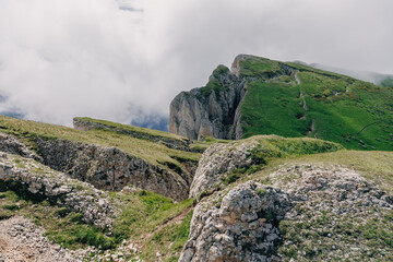 Mountain ridge with green slopes and dramatic cliffs rising above clouds on a moody summer day....