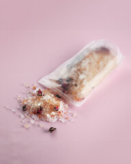 bath salt package lies on a soft pink surface, with some of its contents spilling out. The bath...