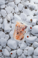 close-up of an aromatic bath salt pouch resting on smooth white stones, surrounded by delicate...