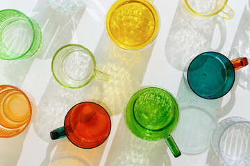 Colorful glowing glass cups on white background, casting artistic light reflections and shadows in...