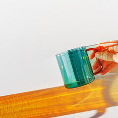 Vibrant still-life with colorful transparent glass mug or cup in shades of green teal and orange....