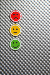 Three round emoji faces in red, yellow, and green representing sad, neutral, and happy emotions on a metallic textured background, symbolizing feedback or mood scale, copy space, vertical
