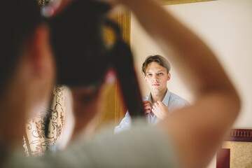 Caucasian man adjusting shirt collar before a photoshoot, seen through photographer’s arms — authentic behind-the-scenes moment showing focus, style, and creative preparation.