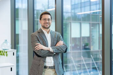 A smiling young man, founder and owner of a firm and company, stands in the lobby of an office...