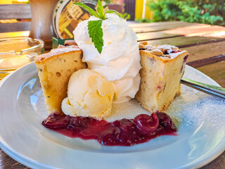 Cherry cake with ice cream and cherries with cream on a large white plate
