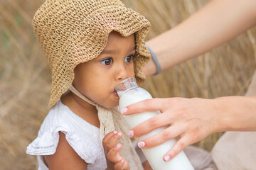 A large portrait of a little mulatto girl who drinks milk from a bottle held by her mother's hands...