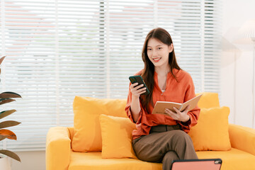 Beautiful Asian woman playing social media using smartphone at home. Woman is shopping and chatting with friends online.
