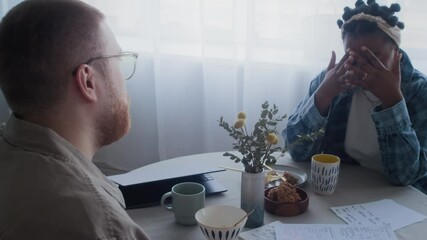 Biracial couple sitting at table in kitchen, arguing about unpaid utility expenses, over shoulder shot - Powered by Adobe