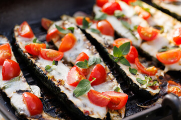 Close up of grilled zucchini stuffed cheese and tomatoes sprinkled with fresh herbs on a grill...