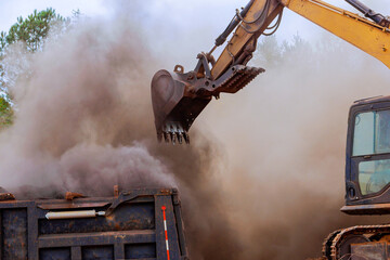 Heavy machinery operates to load construction debris into truck, creating cloud of dust at works...