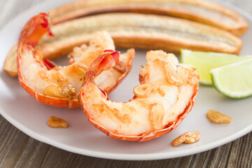 Homemade fried lobster tails with fried garlic slices, lime wedges, and fried green banana slices...